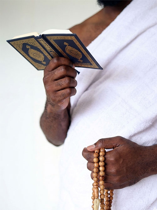 Pilgrim in ihram holding a Quran and prayer beads